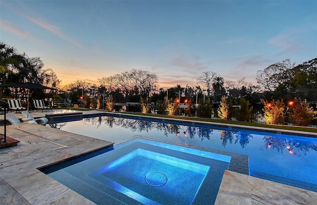 pool at dusk with an in ground hot tub and a patio area