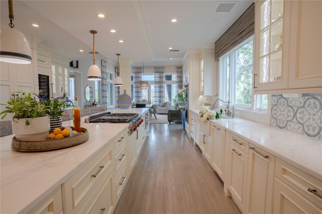 kitchen featuring stainless steel gas cooktop, light stone counters, tasteful backsplash, decorative light fixtures, and light wood-type flooring