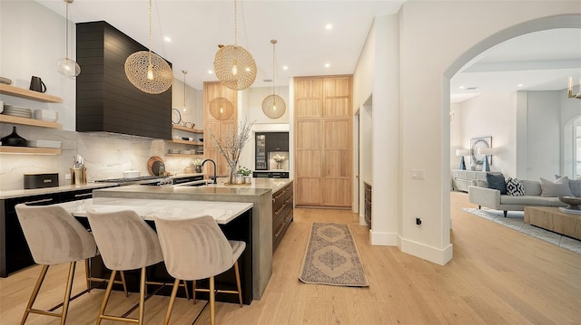 kitchen featuring hanging light fixtures, decorative backsplash, light hardwood / wood-style flooring, a breakfast bar, and an island with sink