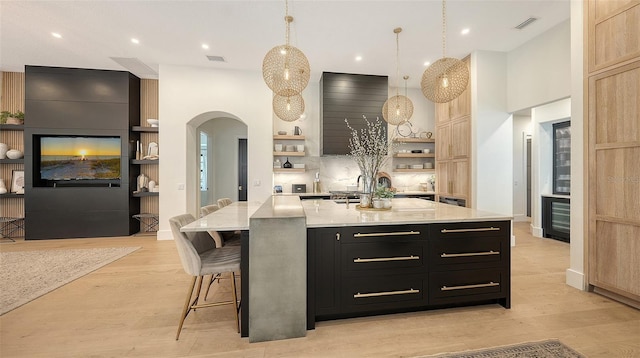 kitchen with light brown cabinetry, a large island with sink, pendant lighting, and light wood-type flooring