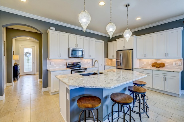 kitchen with decorative light fixtures, white cabinetry, stainless steel appliances, an island with sink, and sink