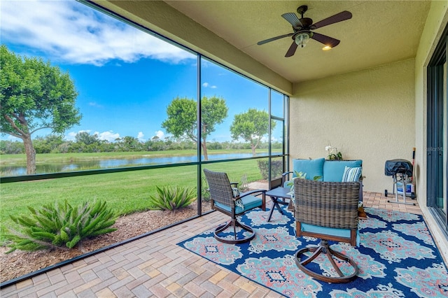 sunroom with ceiling fan and a water view