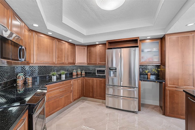 kitchen with a raised ceiling, dark stone counters, and stainless steel appliances