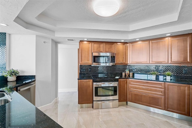 kitchen with appliances with stainless steel finishes, backsplash, dark stone counters, a raised ceiling, and sink