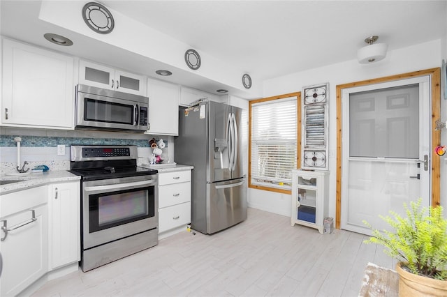 kitchen featuring decorative backsplash, white cabinets, light stone countertops, and appliances with stainless steel finishes