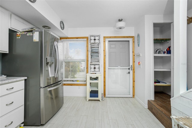 kitchen with stainless steel fridge with ice dispenser, white cabinets, light stone counters, and light hardwood / wood-style floors