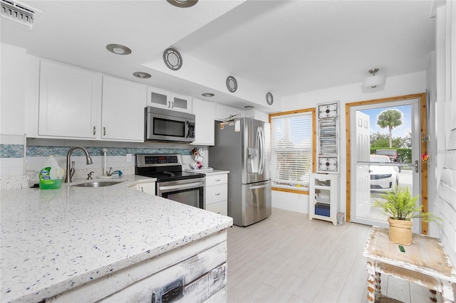 kitchen featuring appliances with stainless steel finishes, tasteful backsplash, light stone counters, sink, and white cabinetry