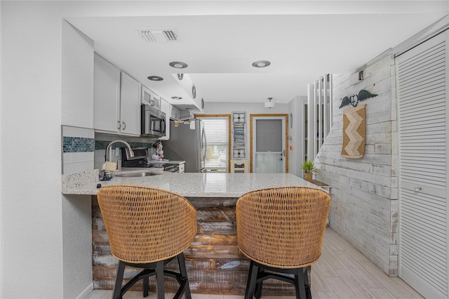 kitchen featuring kitchen peninsula, appliances with stainless steel finishes, sink, white cabinetry, and a breakfast bar area