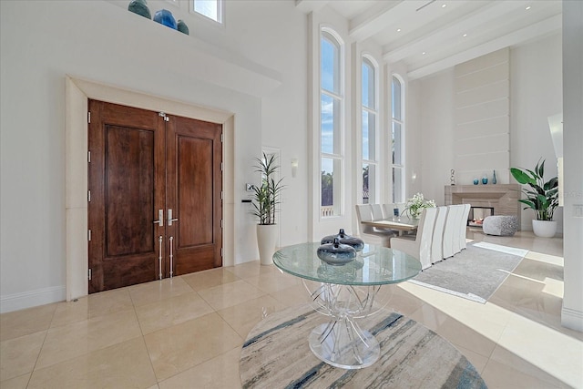 foyer entrance featuring a towering ceiling, a multi sided fireplace, light tile patterned floors, and beamed ceiling