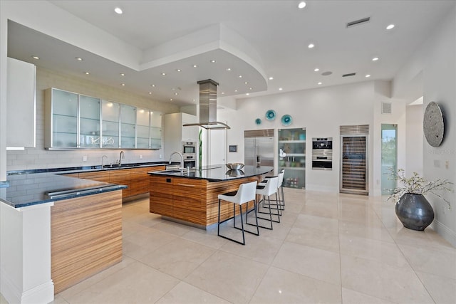 kitchen with stainless steel built in refrigerator, island exhaust hood, light tile patterned floors, and a spacious island