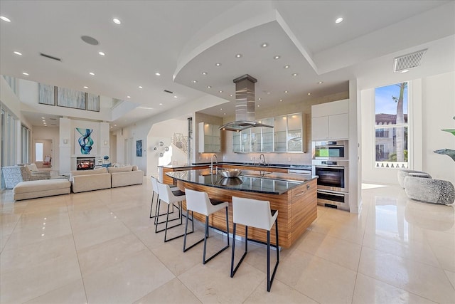 kitchen featuring white cabinetry, light tile patterned flooring, stainless steel double oven, island range hood, and a breakfast bar