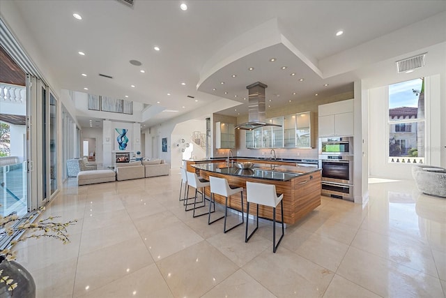 kitchen featuring a breakfast bar, light tile patterned floors, island exhaust hood, white cabinetry, and stainless steel double oven