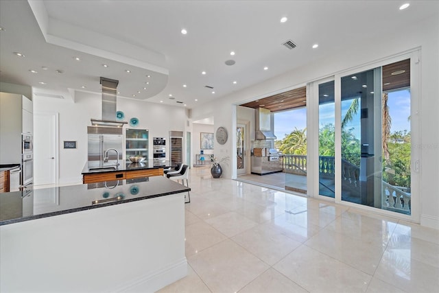 kitchen featuring island range hood, light tile patterned floors, white cabinetry, appliances with stainless steel finishes, and sink