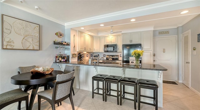 kitchen with black appliances, crown molding, light tile patterned floors, a kitchen bar, and kitchen peninsula