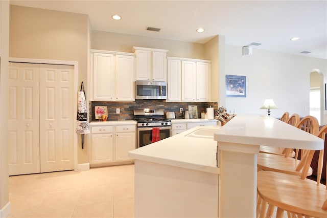 kitchen featuring a breakfast bar area, white cabinetry, light tile patterned floors, stainless steel appliances, and backsplash