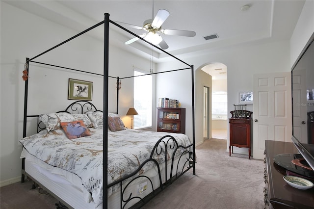 bedroom featuring connected bathroom, a tray ceiling, ceiling fan, and carpet