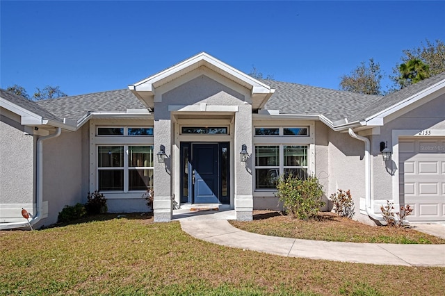 view of front facade featuring a front lawn, roof with shingles, an attached garage, and stucco siding