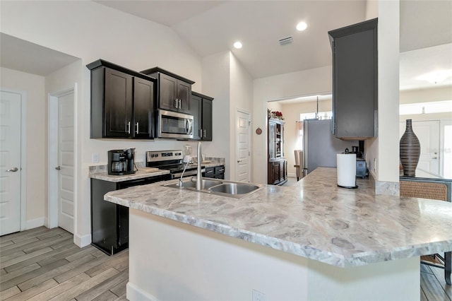 kitchen featuring stainless steel appliances, a peninsula, visible vents, vaulted ceiling, and light wood-type flooring