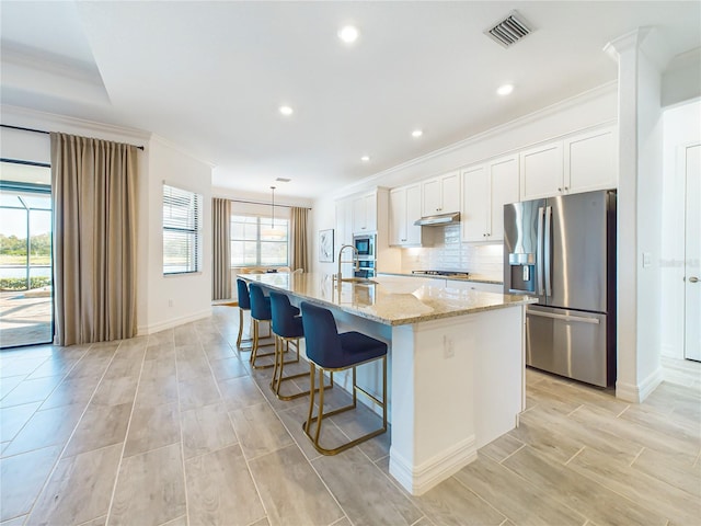 kitchen featuring white cabinets, appliances with stainless steel finishes, an island with sink, and ornamental molding