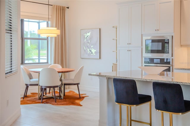 kitchen with stainless steel appliances, white cabinets, hanging light fixtures, and light stone countertops