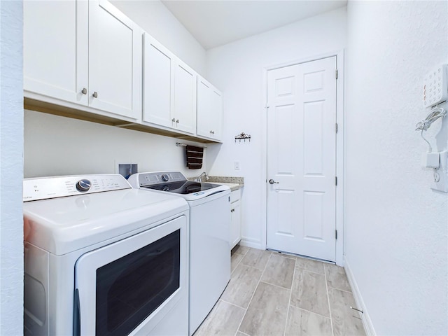 clothes washing area featuring washing machine and dryer, cabinets, and light hardwood / wood-style floors