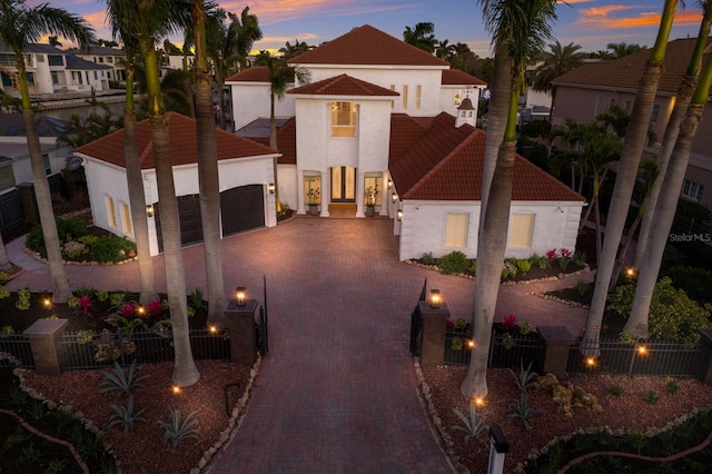 mediterranean / spanish home with a fenced front yard, decorative driveway, stucco siding, a garage, and a tiled roof