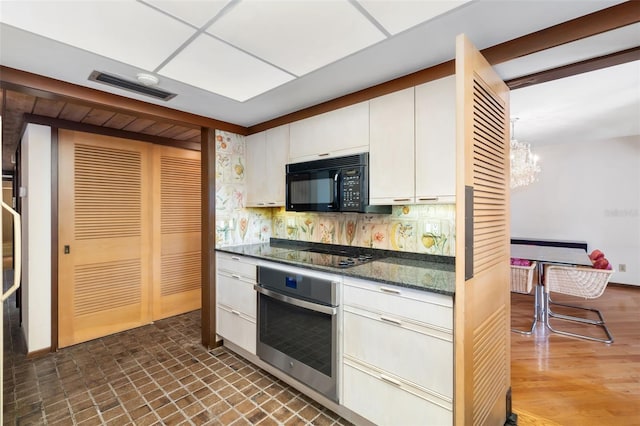 kitchen featuring black appliances, white cabinets, decorative backsplash, dark stone countertops, and a chandelier