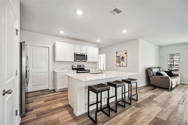 kitchen featuring a breakfast bar area, light hardwood / wood-style flooring, white cabinetry, stainless steel appliances, and a center island with sink