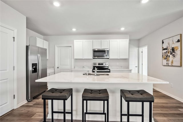 kitchen featuring white cabinetry, appliances with stainless steel finishes, dark hardwood / wood-style flooring, an island with sink, and light stone countertops