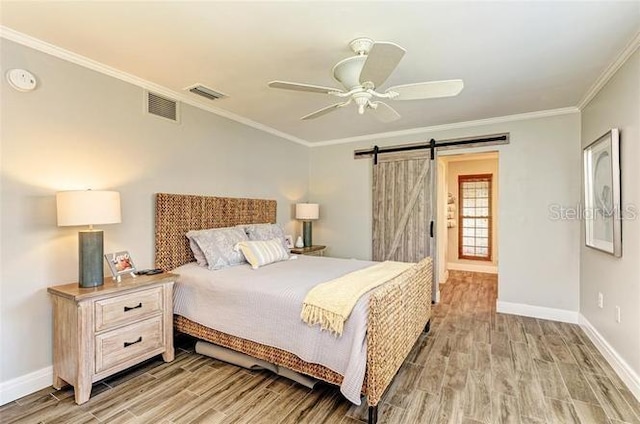 bedroom featuring ceiling fan, a barn door, light hardwood / wood-style floors, and crown molding