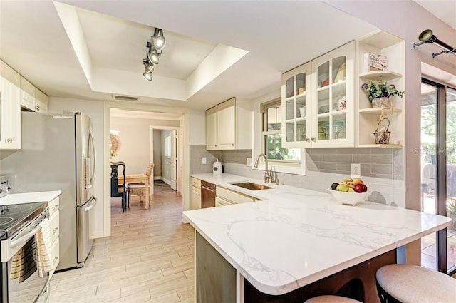 kitchen with sink, kitchen peninsula, stainless steel appliances, and a tray ceiling