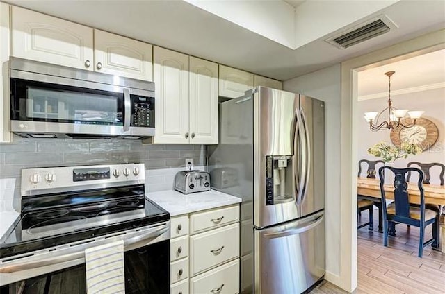 kitchen with white cabinets, decorative backsplash, stainless steel appliances, and a notable chandelier