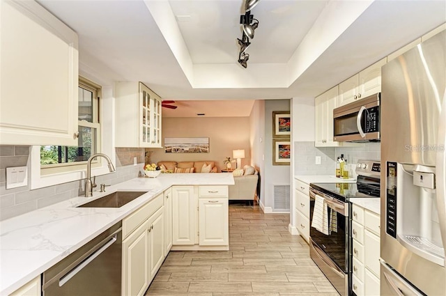 kitchen featuring kitchen peninsula, appliances with stainless steel finishes, light stone counters, a raised ceiling, and sink