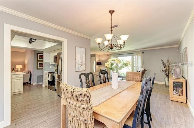 dining area with light wood-type flooring, crown molding, a tray ceiling, and a chandelier