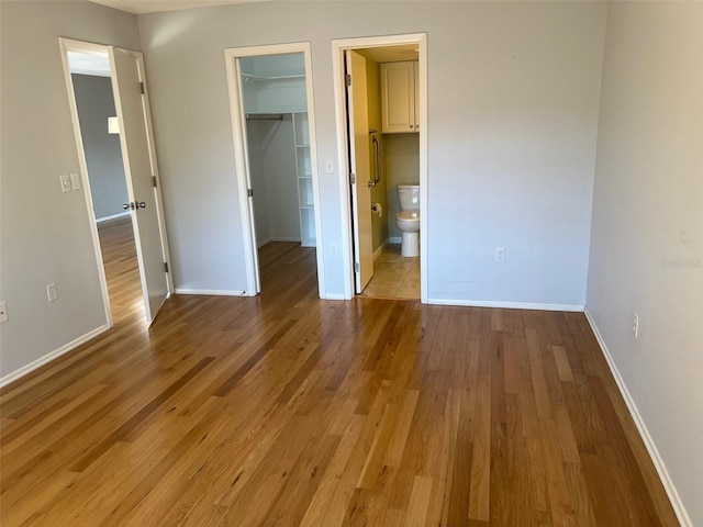 unfurnished bedroom with ensuite bathroom, a spacious closet, a closet, and light wood-type flooring