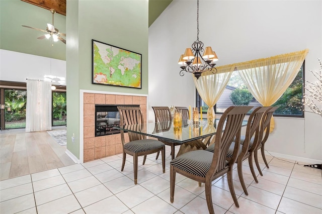 tiled dining space featuring ceiling fan with notable chandelier, a fireplace, and a high ceiling