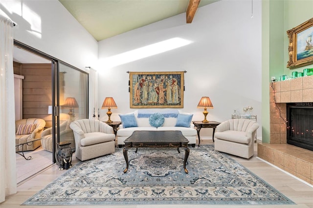 living area with vaulted ceiling with beams, light wood-type flooring, and a tiled fireplace