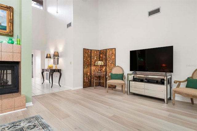 living area with a tiled fireplace, a towering ceiling, and light hardwood / wood-style floors