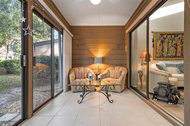 living area featuring light tile patterned floors, ceiling fan, ornamental molding, and wood walls