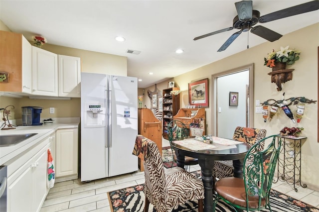 kitchen featuring dishwasher, white refrigerator with ice dispenser, sink, ceiling fan, and white cabinetry