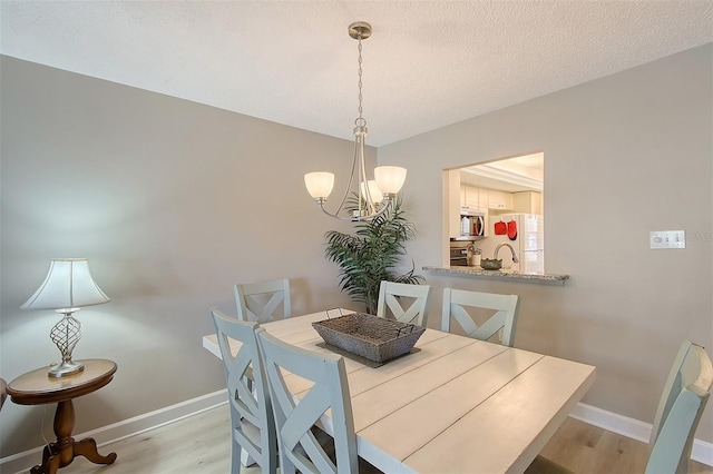 dining area featuring a textured ceiling, an inviting chandelier, and light hardwood / wood-style flooring