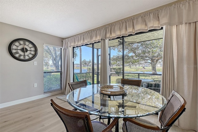 dining space with a water view, a textured ceiling, and light hardwood / wood-style flooring