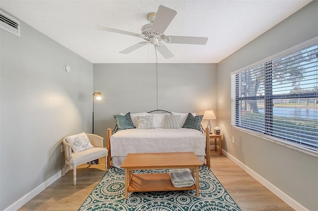 bedroom with ceiling fan, light hardwood / wood-style floors, and a textured ceiling