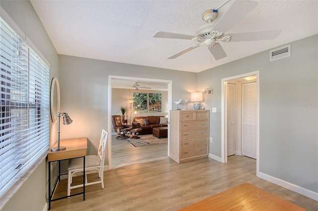 interior space with ceiling fan, a textured ceiling, and light wood-type flooring