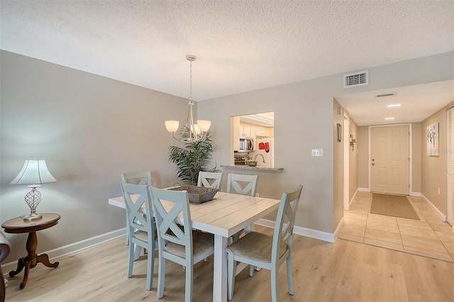 dining space with an inviting chandelier, a textured ceiling, and light wood-type flooring