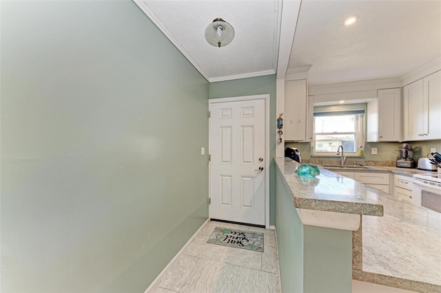 kitchen featuring sink, light tile patterned floors, kitchen peninsula, white cabinets, and ornamental molding