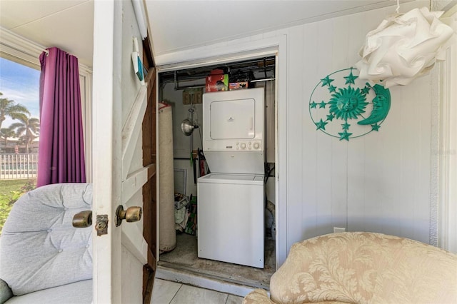 laundry room featuring wooden walls, light tile patterned floors, and stacked washer / drying machine