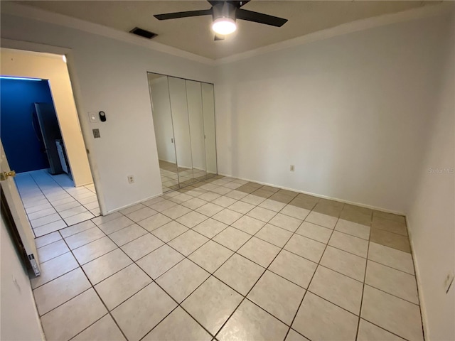 unfurnished bedroom with ceiling fan, a closet, light tile patterned floors, and ornamental molding