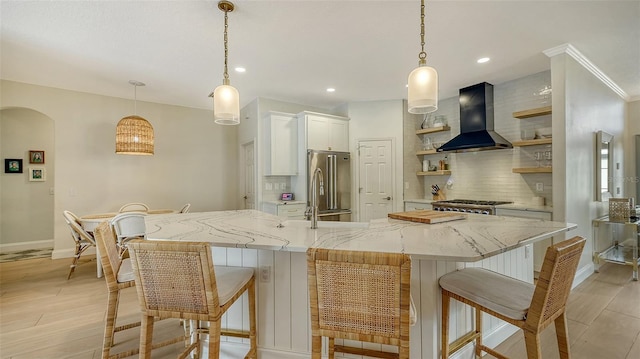 kitchen featuring white cabinetry, high end refrigerator, wall chimney exhaust hood, and decorative light fixtures