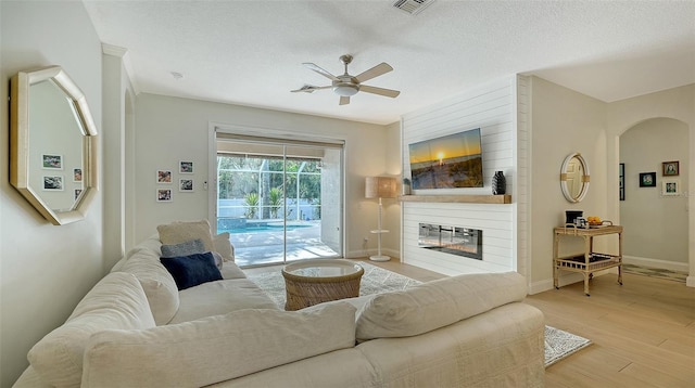 living room featuring a fireplace, a textured ceiling, light hardwood / wood-style flooring, and ceiling fan